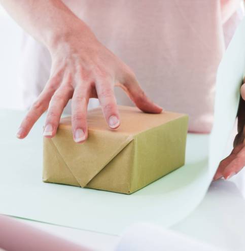 close-up-woman-wrapping-gift-box-with-paper-table